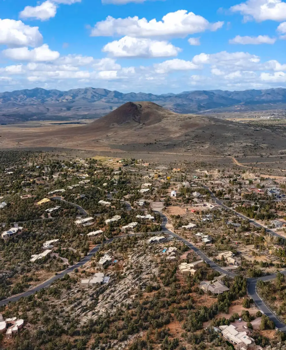 Aerial view of a high-desert community with scattered homes, juniper scrub and a prominent cone-shaped hill against distant mountains.