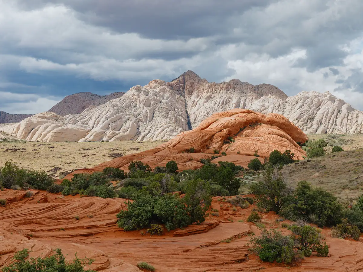Snow Canyon striated red sandstone domes meeting white petrified dunes under a moody cloudy sky near Entrada, Utah.