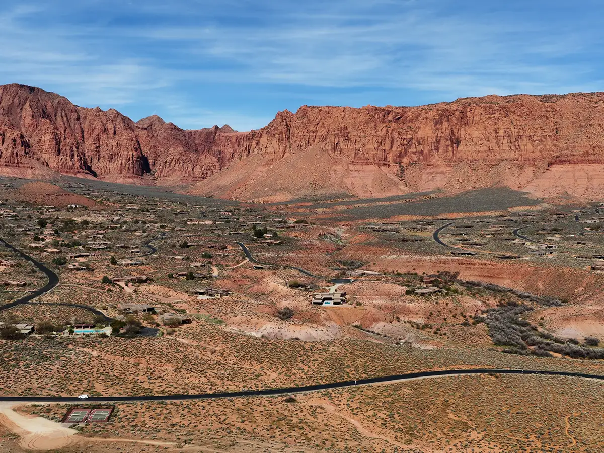 Aerial view of Kayenta art village homes blended into the red desert below towering cliffs in Ivins, Utah.