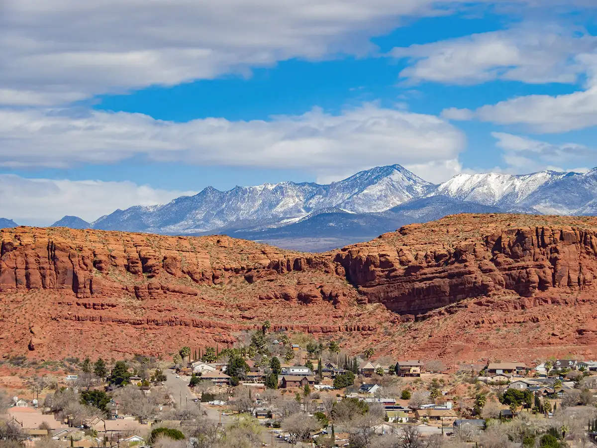 Stone Cliffs neighborhood backed by red sandstone bluffs and snow-capped Pine Valley Mountains in St. George, Utah.