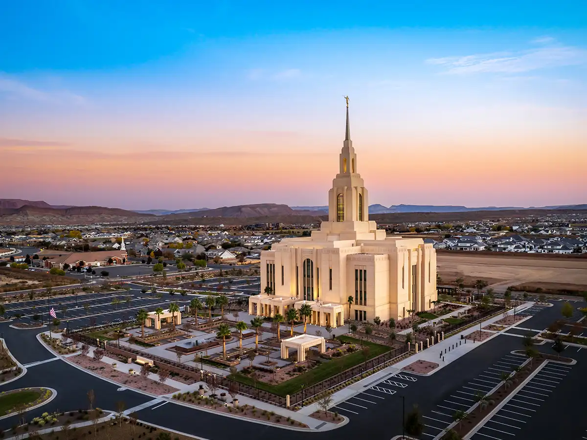 Red Cliffs Utah Temple illuminated at sunset with surrounding gardens and the Summit View community in the foothills.