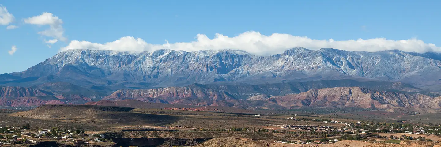 Snow-capped mountain range rising above red rock foothills and a residential valley near St. George, Utah.