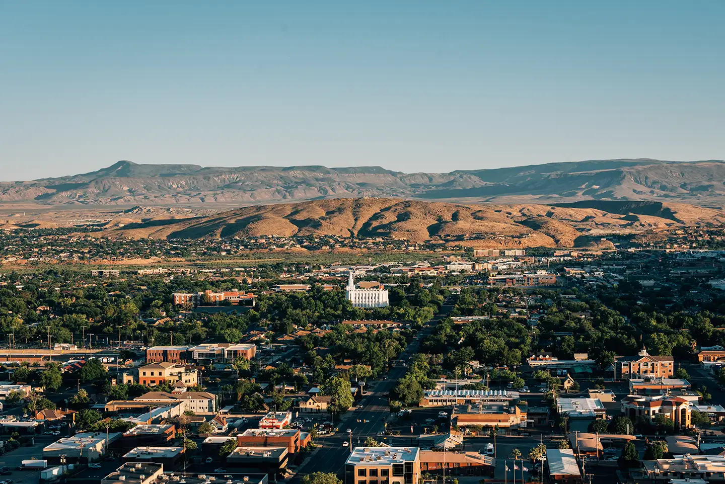 Elevated view of downtown St. George at golden hour, anchored by the white historic temple and framed by surrounding desert ridges.