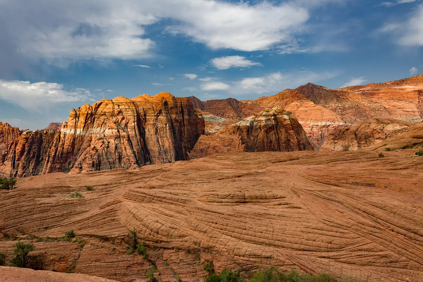 Petrified sandstone dunes and rust-colored cliffs in Snow Canyon State Park under a sky scattered with white clouds.