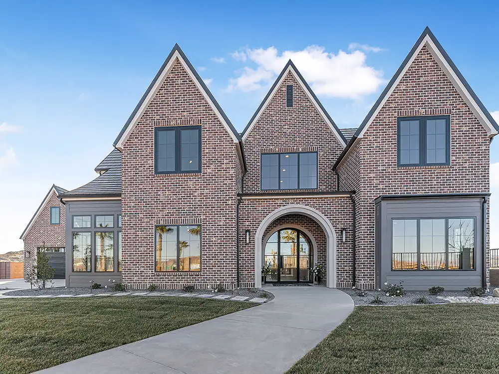 Tudor-style brick home with three steep gables, arched front entry and manicured lawn under blue sky.