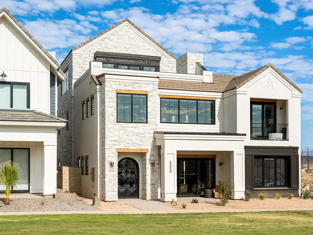 Two-story stone and white modern farmhouse with arched entry under blue sky with scattered clouds.