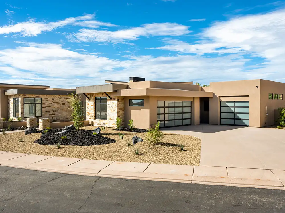 Single-story desert contemporary home with stone accents, glass garage doors and xeriscaped front yard.