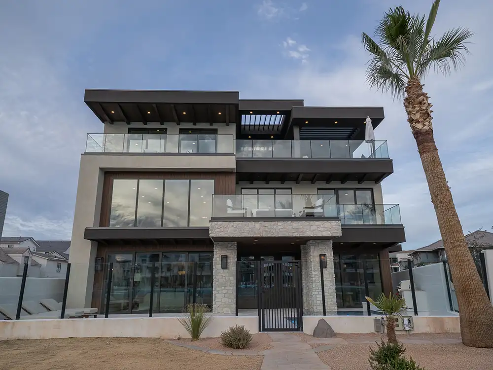 Modern three-story home with wood-trim balconies, stone columns, glass railings and a tall palm tree.