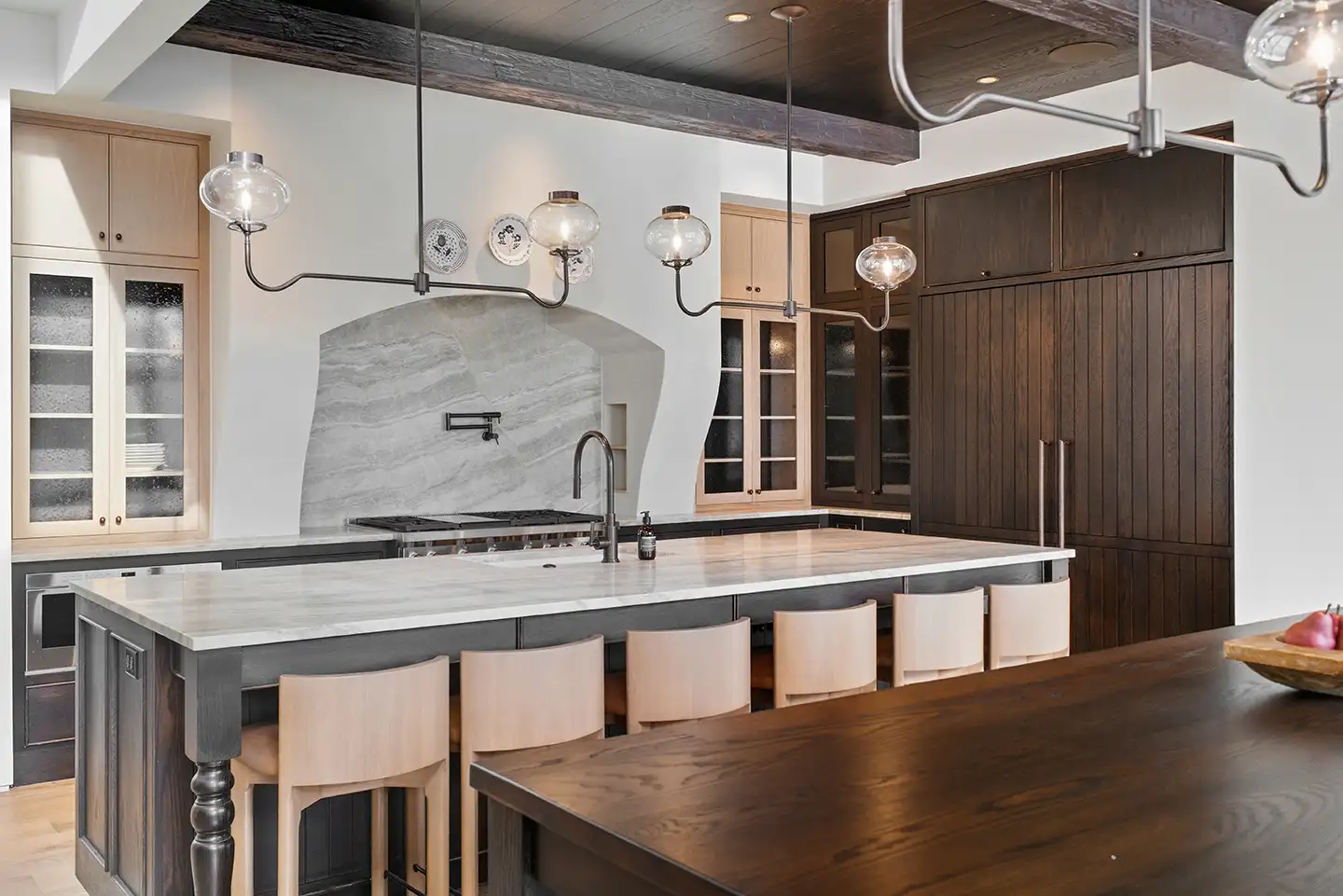 Kitchen with marble waterfall island, light wood barstools, dark cabinetry, marble range hood, and curved glass pendant lights.