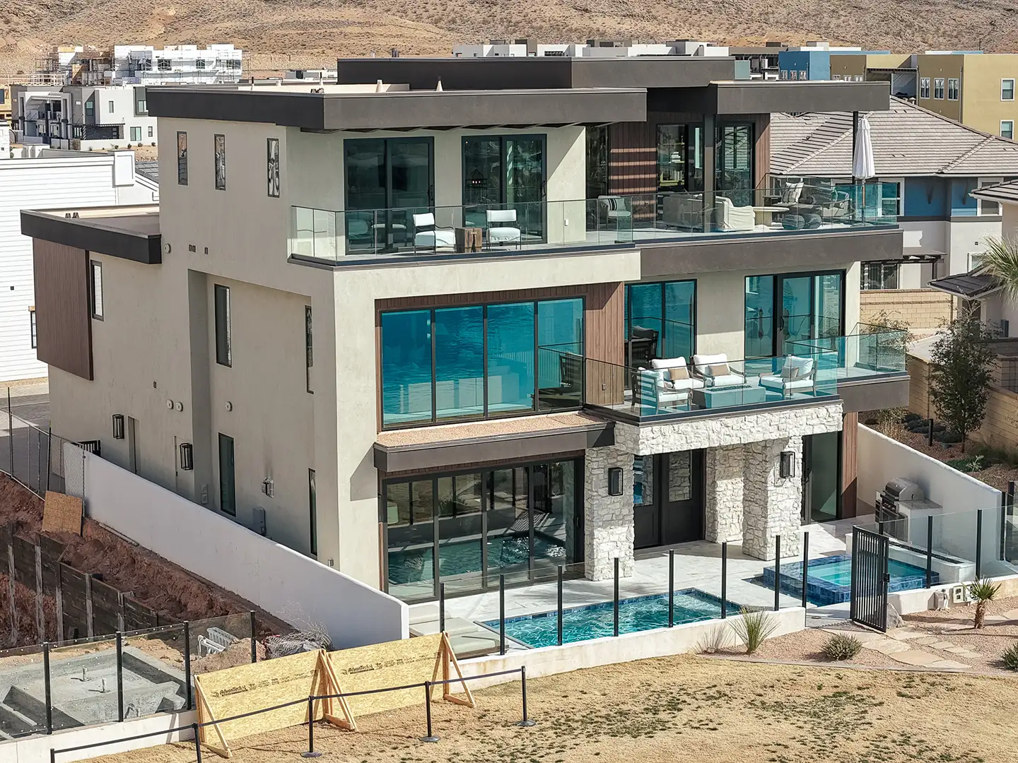 Rear exterior of a modern three-story home with glass balconies, stone accents, and a swimming pool below the patio.