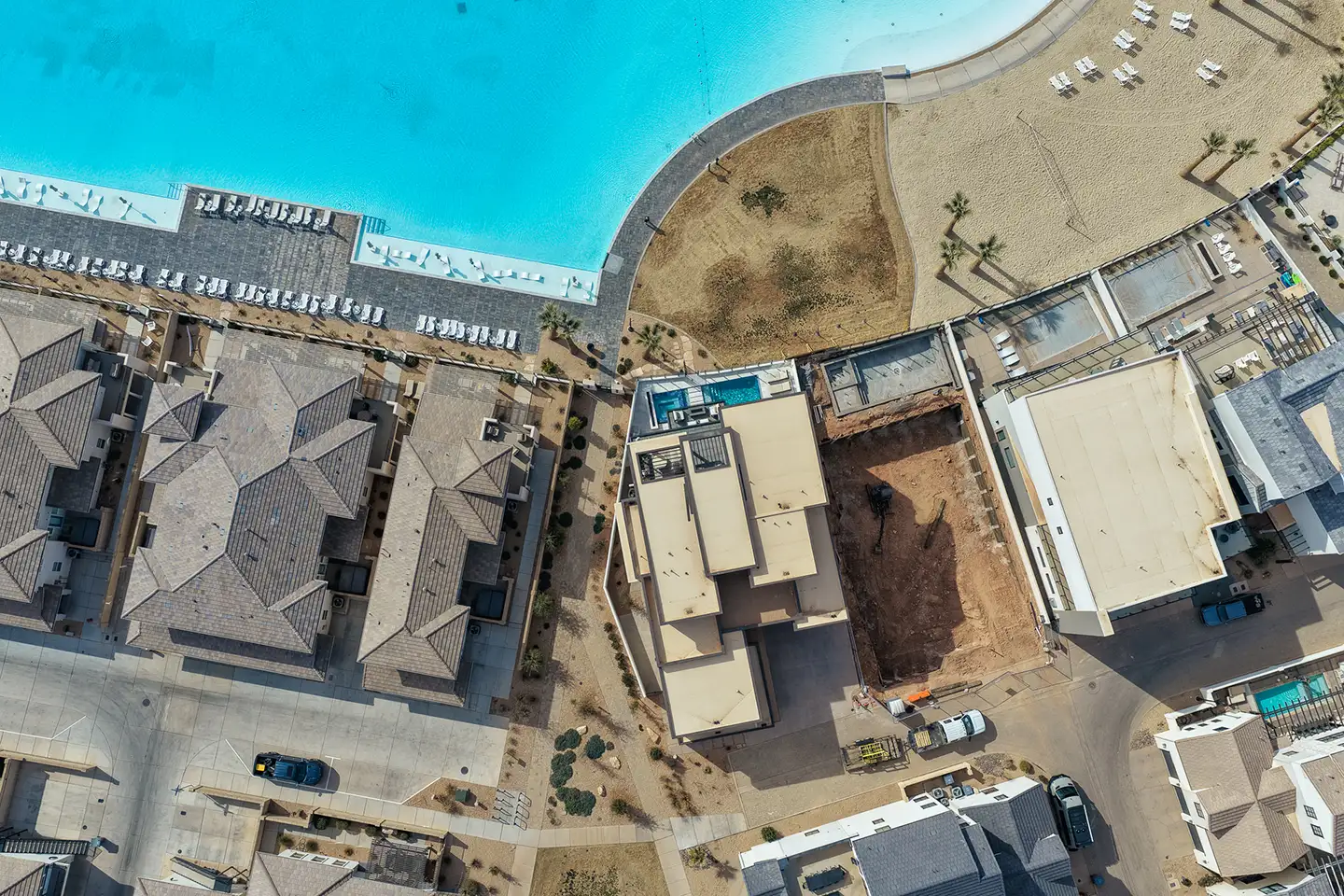 Aerial top-down view of waterfront homes beside turquoise water with a construction lot in the foreground.