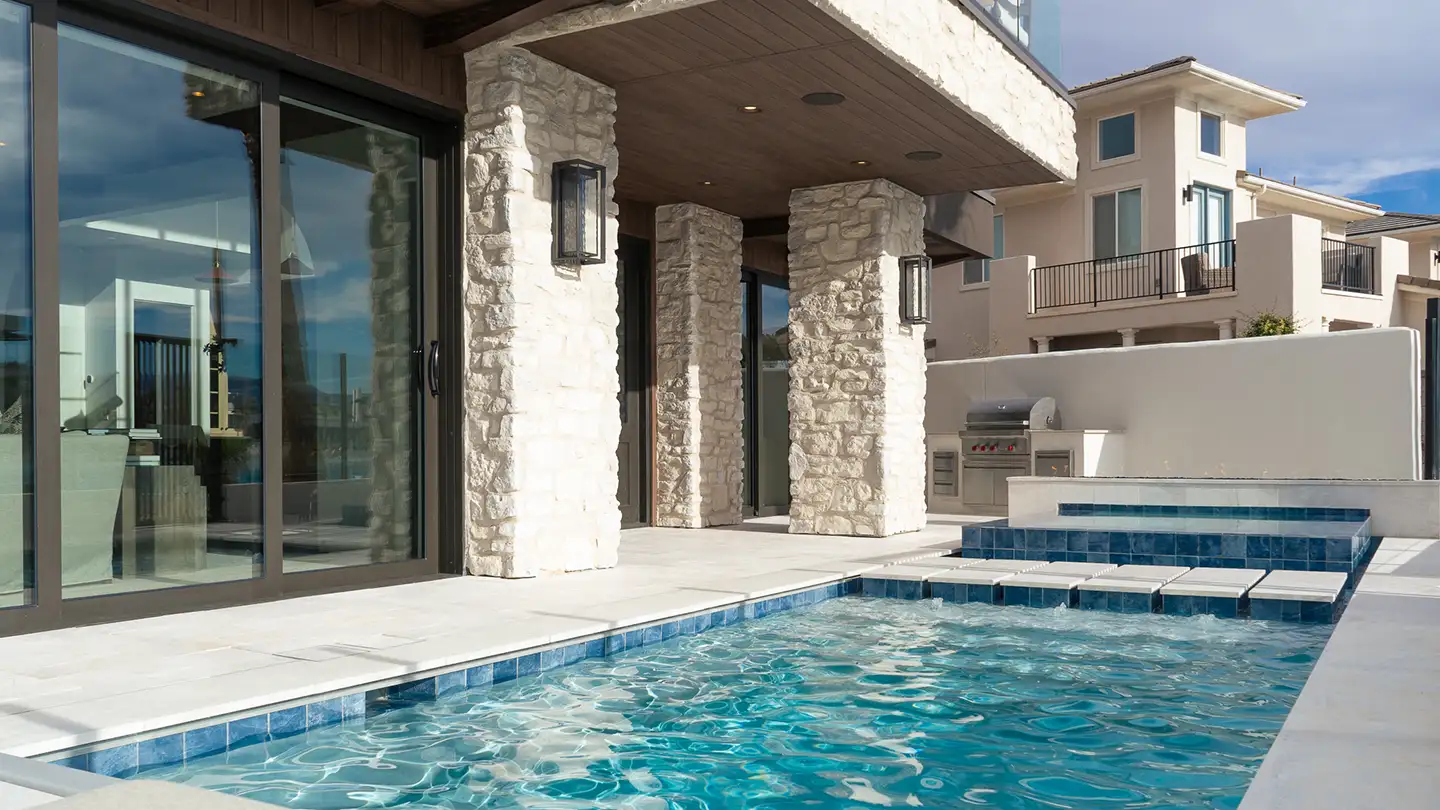 Outdoor pool with stone column patio, sliding glass doors to the interior, and a built-in stainless steel grill area.