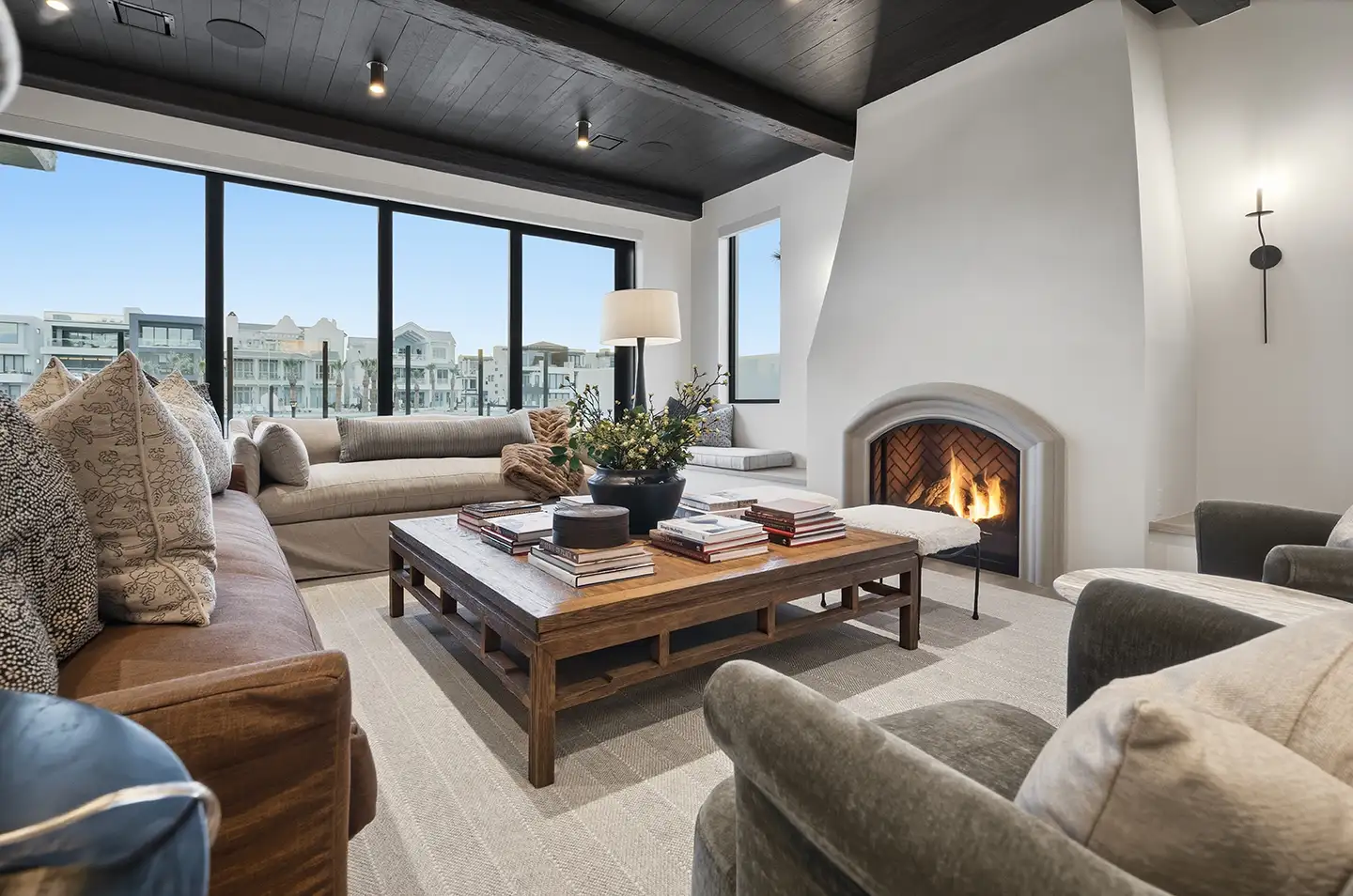 Living room with an arched plaster fireplace, large wood coffee table stacked with books, beige sectional, and tall windows.