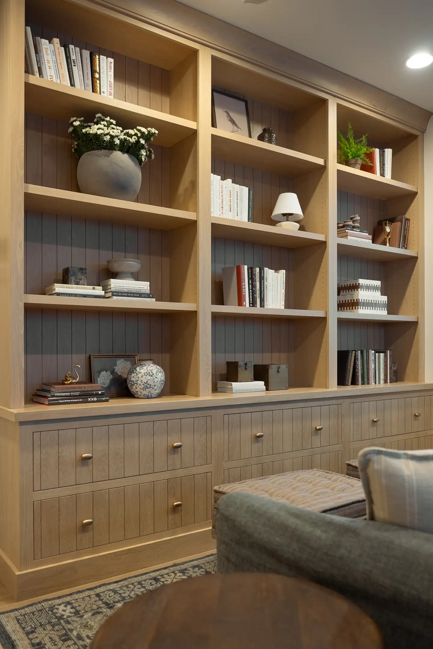 Built-in light wood bookshelves filled with books, plants, and decorative objects styled across multiple shelves above drawers.