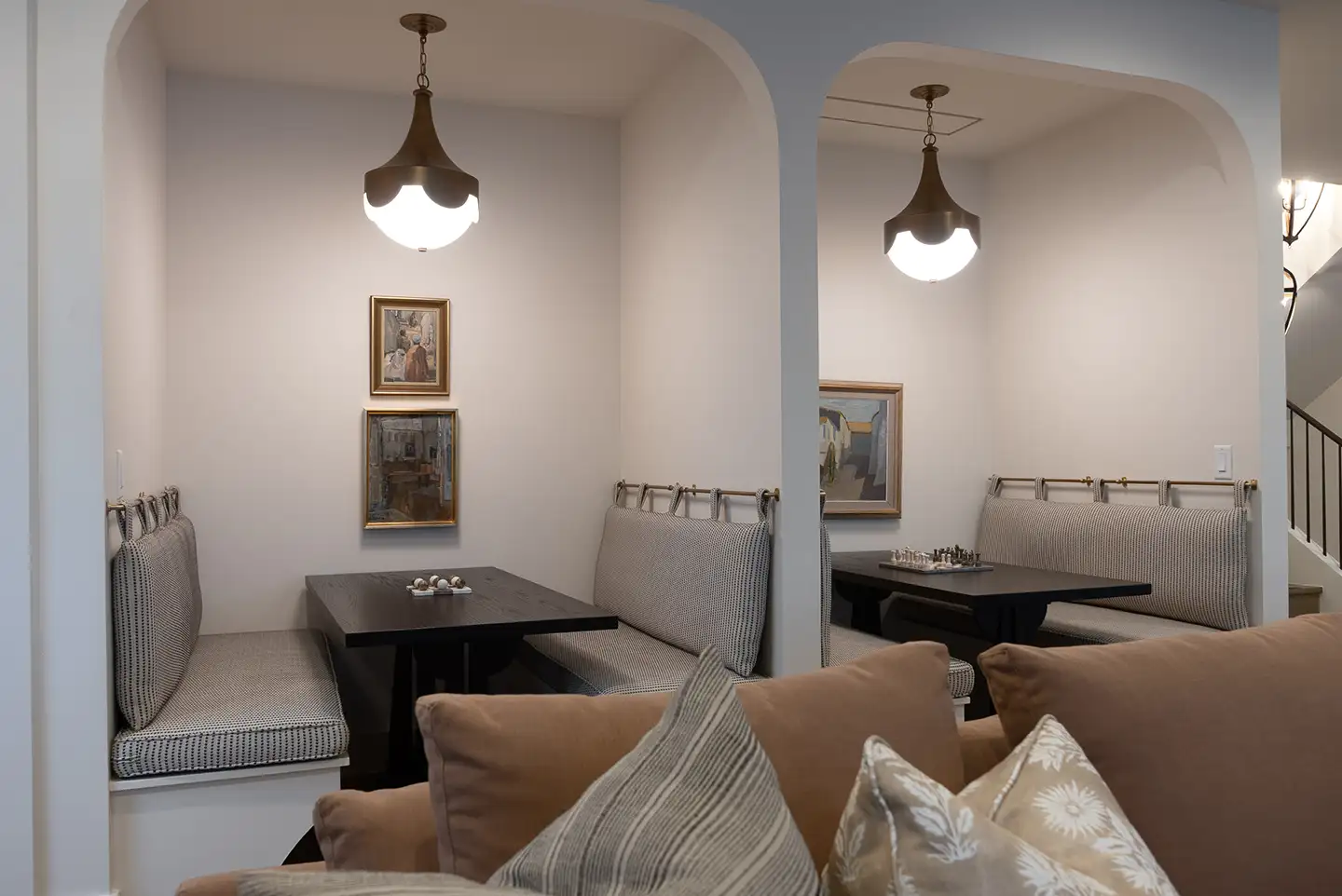 Cushioned banquette dining nook with a dark wood table, framed artwork on the wall, and a pendant light inside an archway.