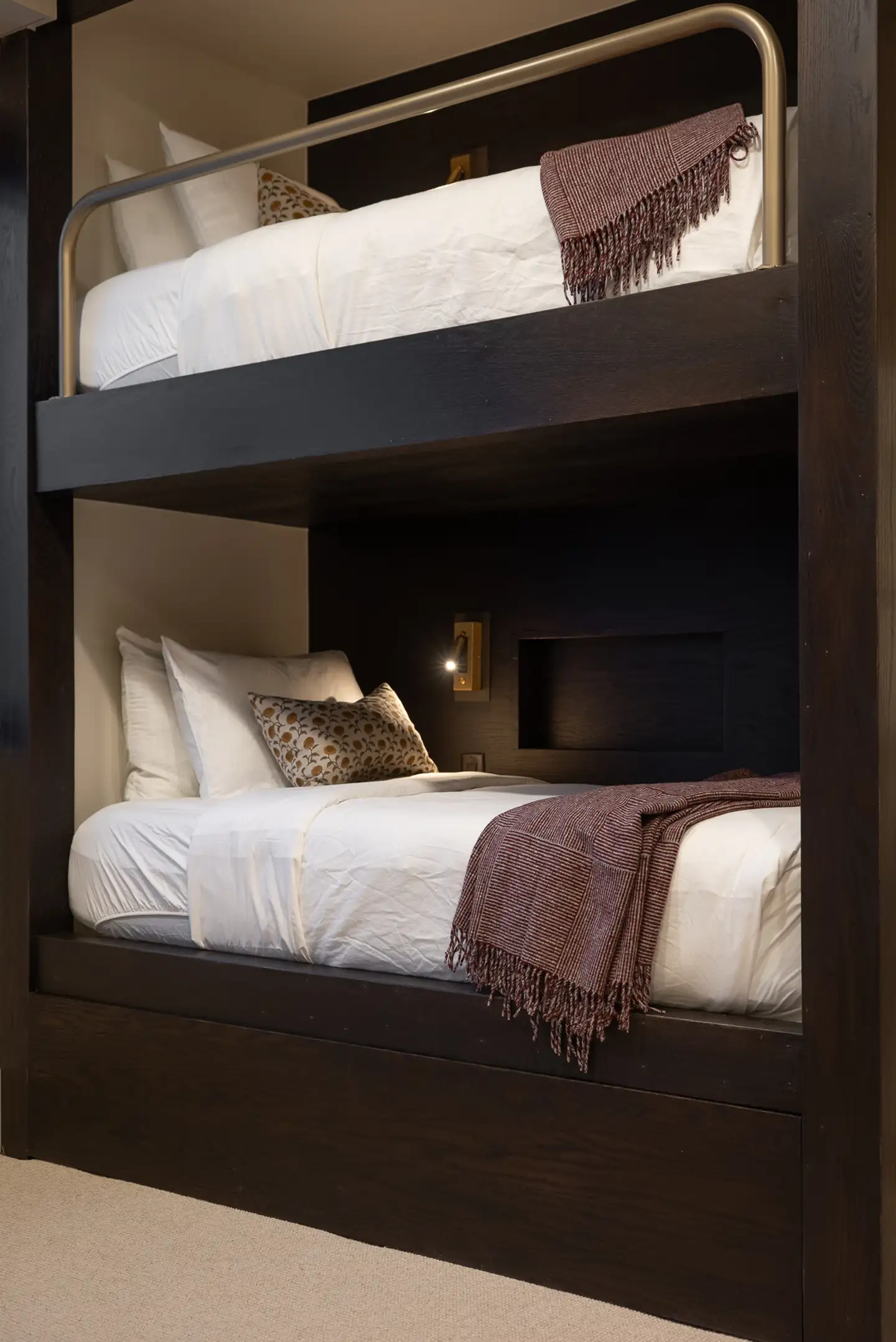 Built-in bunk beds in dark wood with crisp white bedding, a patterned accent pillow, and a fringed burgundy throw blanket.
