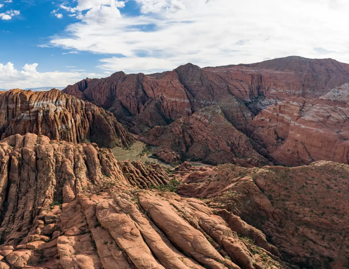 Layered red and white striped sandstone formations carved into ridges and deep canyons under a partly cloudy sky