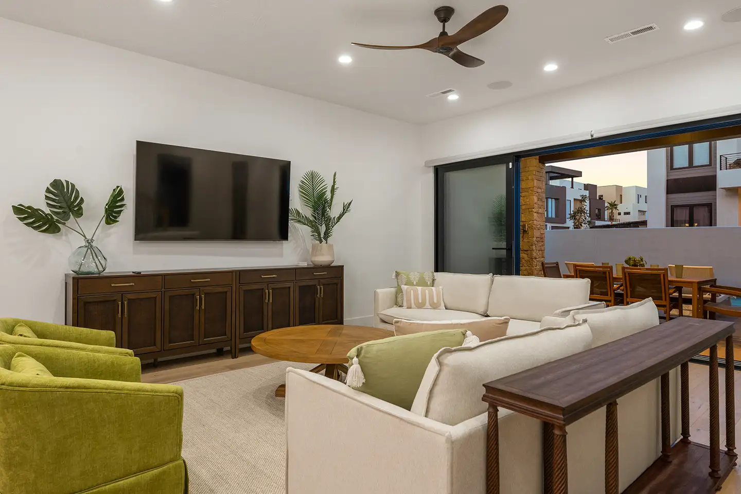 Living room with a sectional sofa and TV opening through sliding doors to an outdoor patio and dining area.