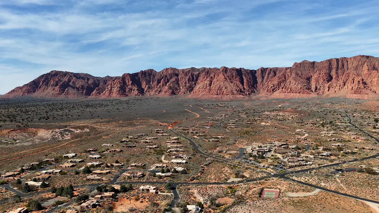 Aerial view of a desert residential community spread below red rock cliffs.