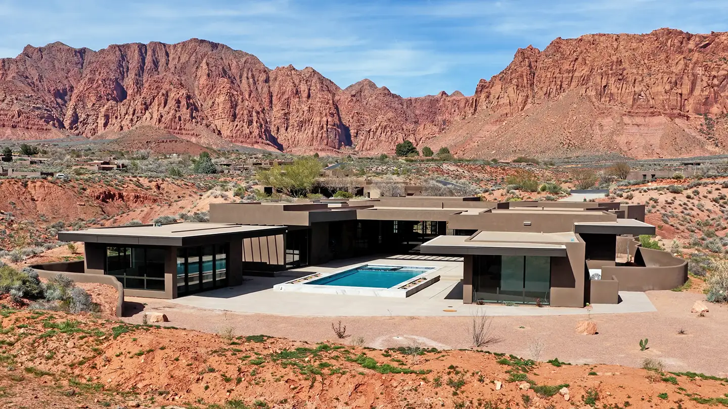 Low-profile modern desert home with a pool set against red rock cliffs and natural landscape.