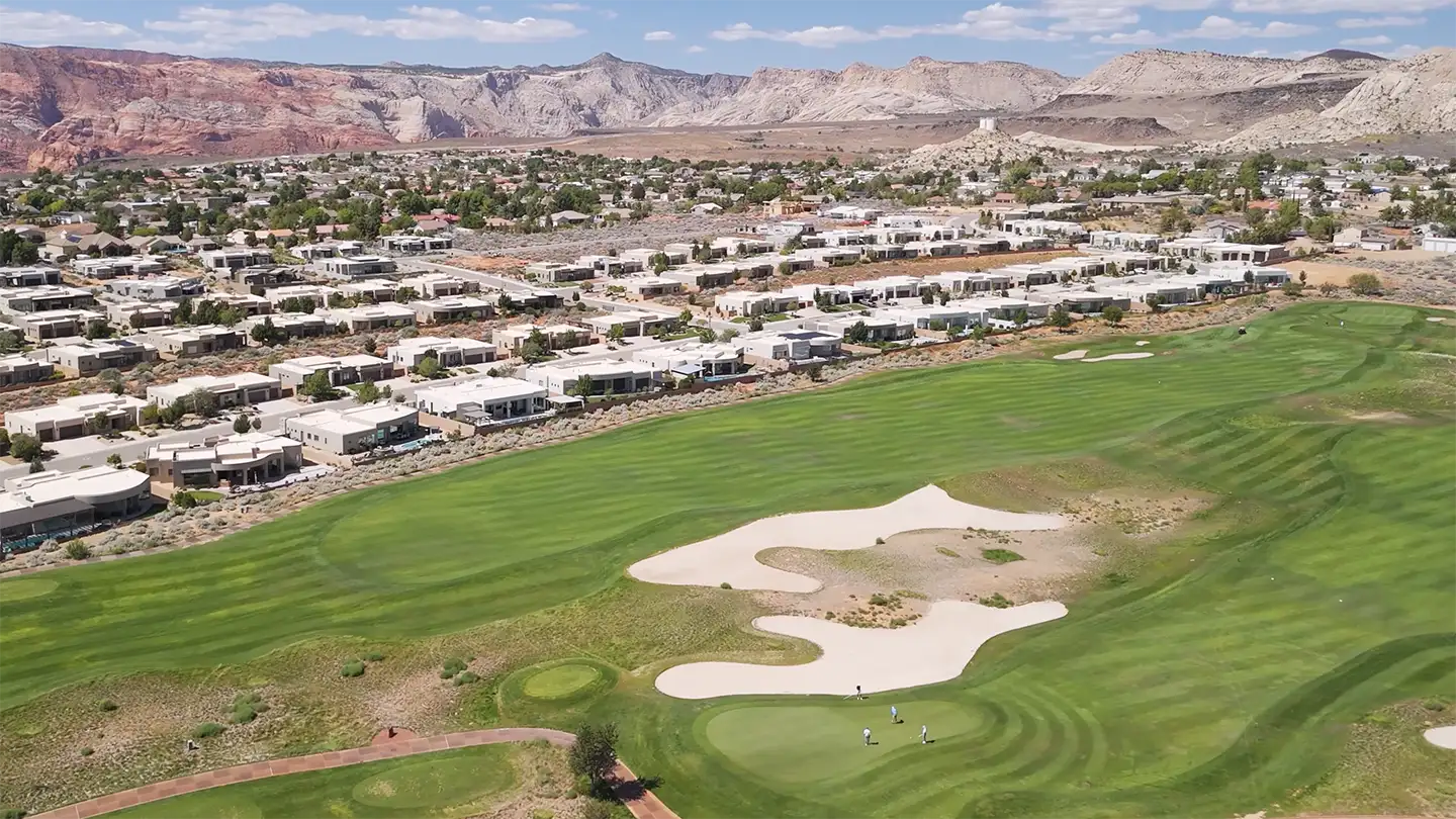 Aerial view of a golf course lined with homes and desert mountains in the background.