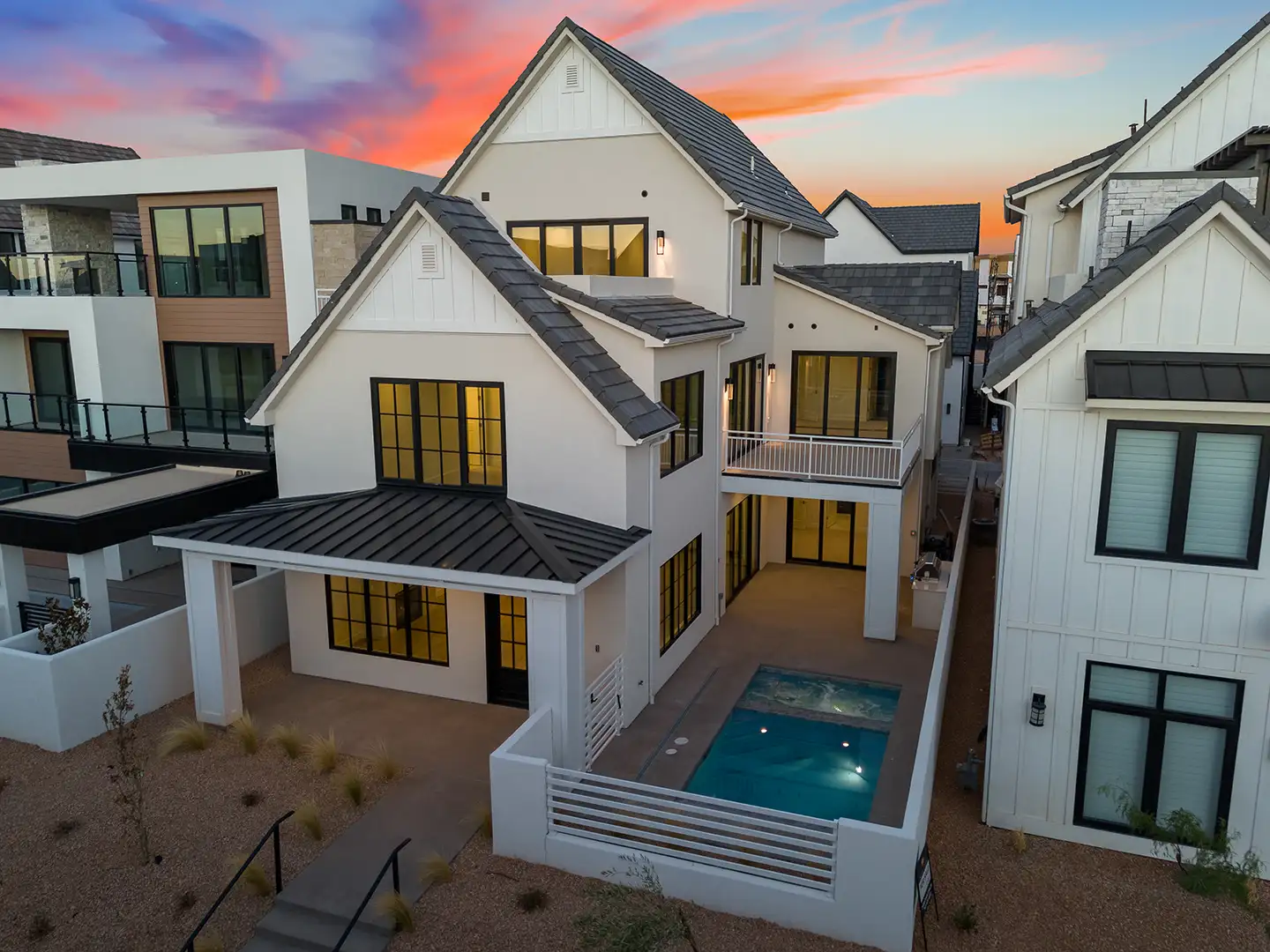Rear exterior of white modern farmhouse-style luxury homes with a pool at sunset.