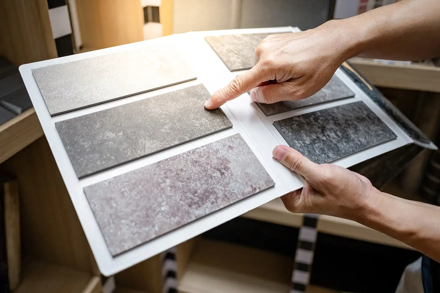 Hands selecting from stone-look tile samples on a board while choosing finishes for a home.