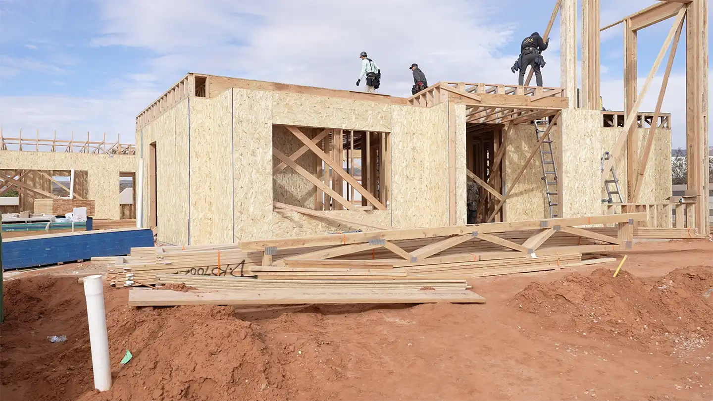 Construction crew framing the walls and roof of a custom home with lumber stacked on the desert lot.
