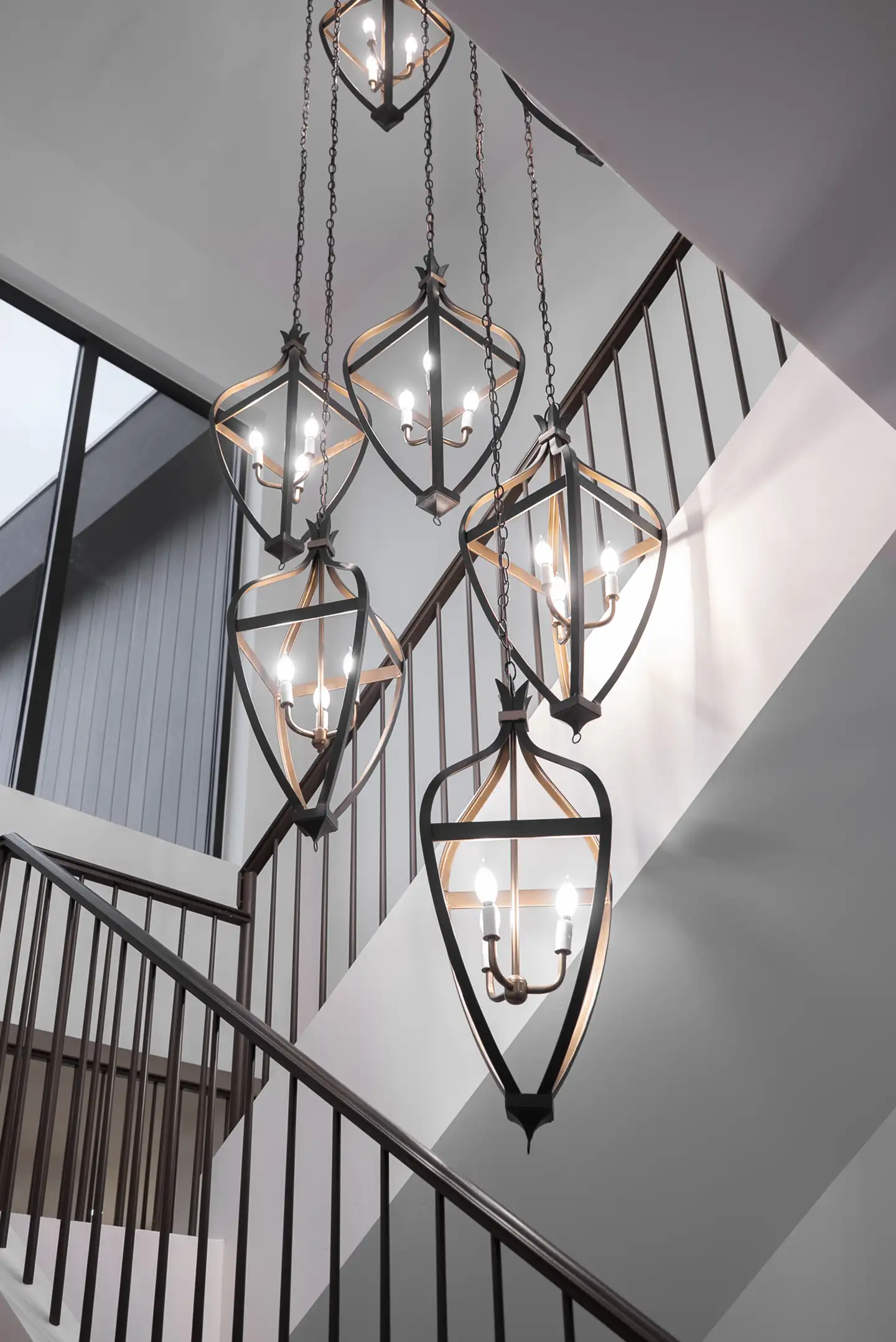 Cluster of black and gold iron lantern pendant lights hanging over a staircase with metal railings in a luxury home.
