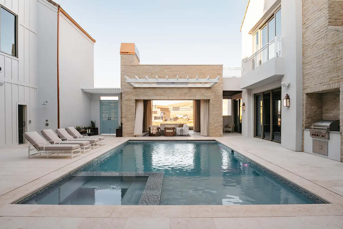 Backyard pool and spa beside a covered patio with lounge chairs and a built-in outdoor grill at a luxury home.
