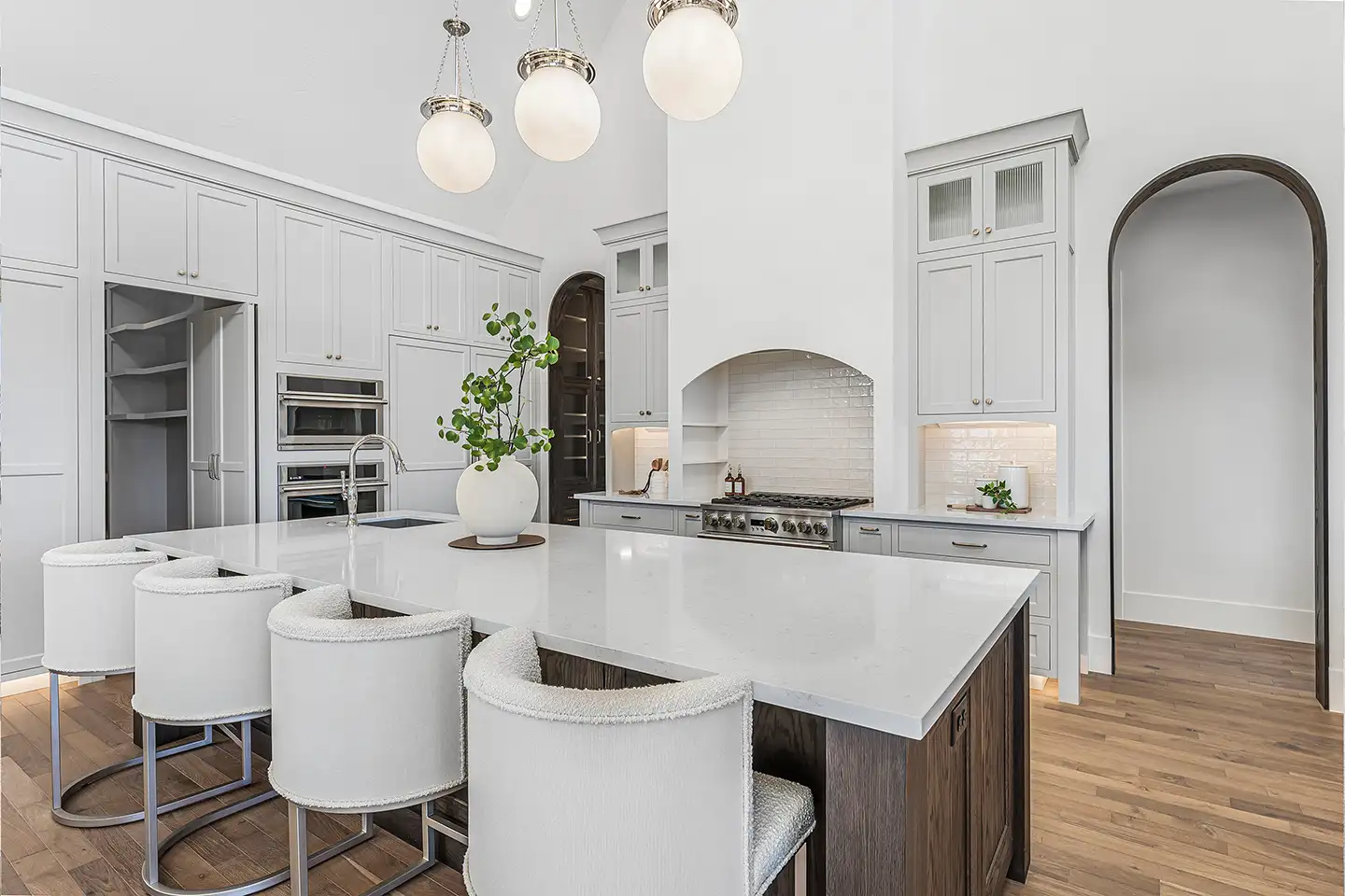 Bright white luxury kitchen with a large quartz island, boucle bar stools, globe pendant lights and a professional range.