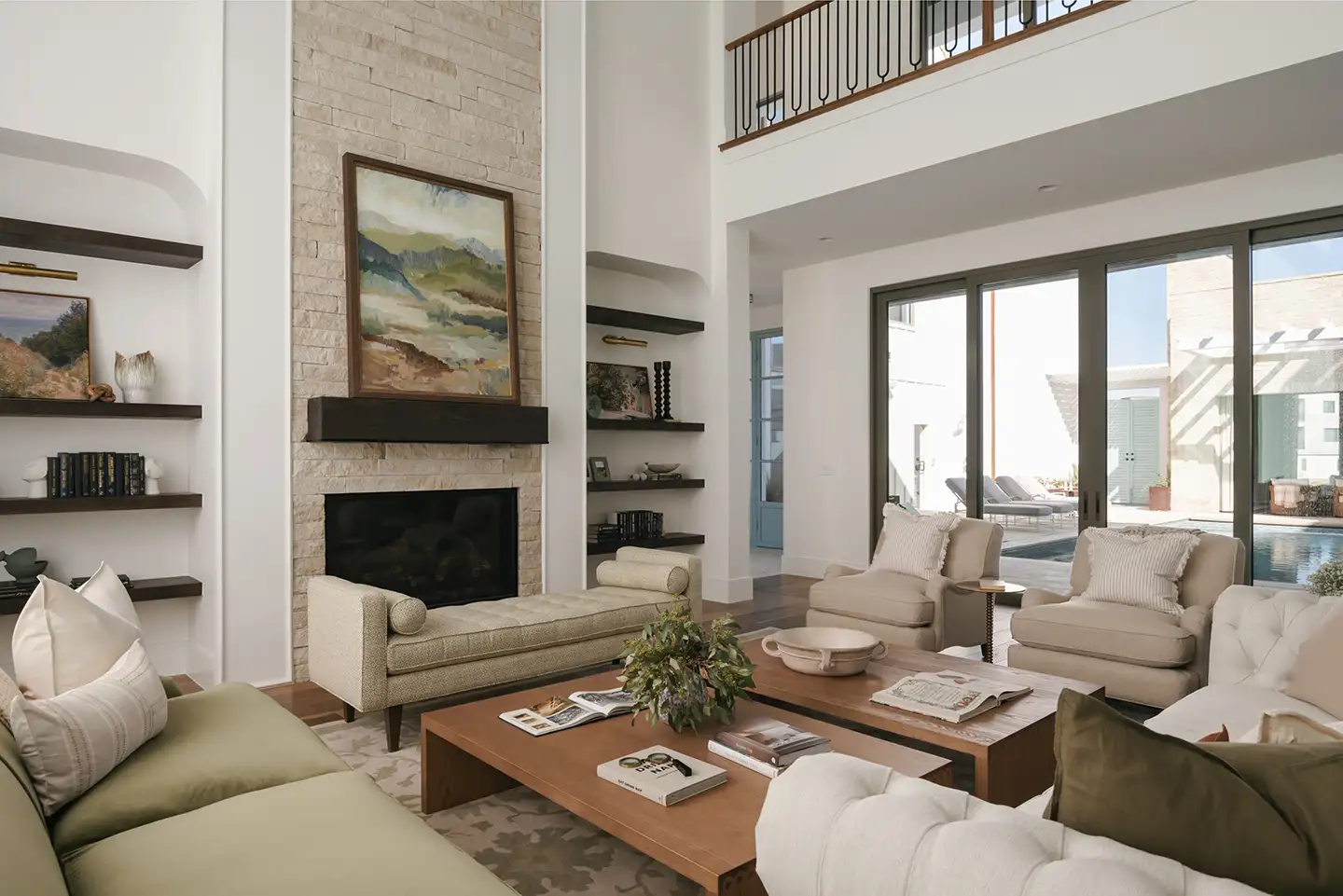 Two-story great room with a floor-to-ceiling stone fireplace and sliding glass doors opening to a covered patio and pool.