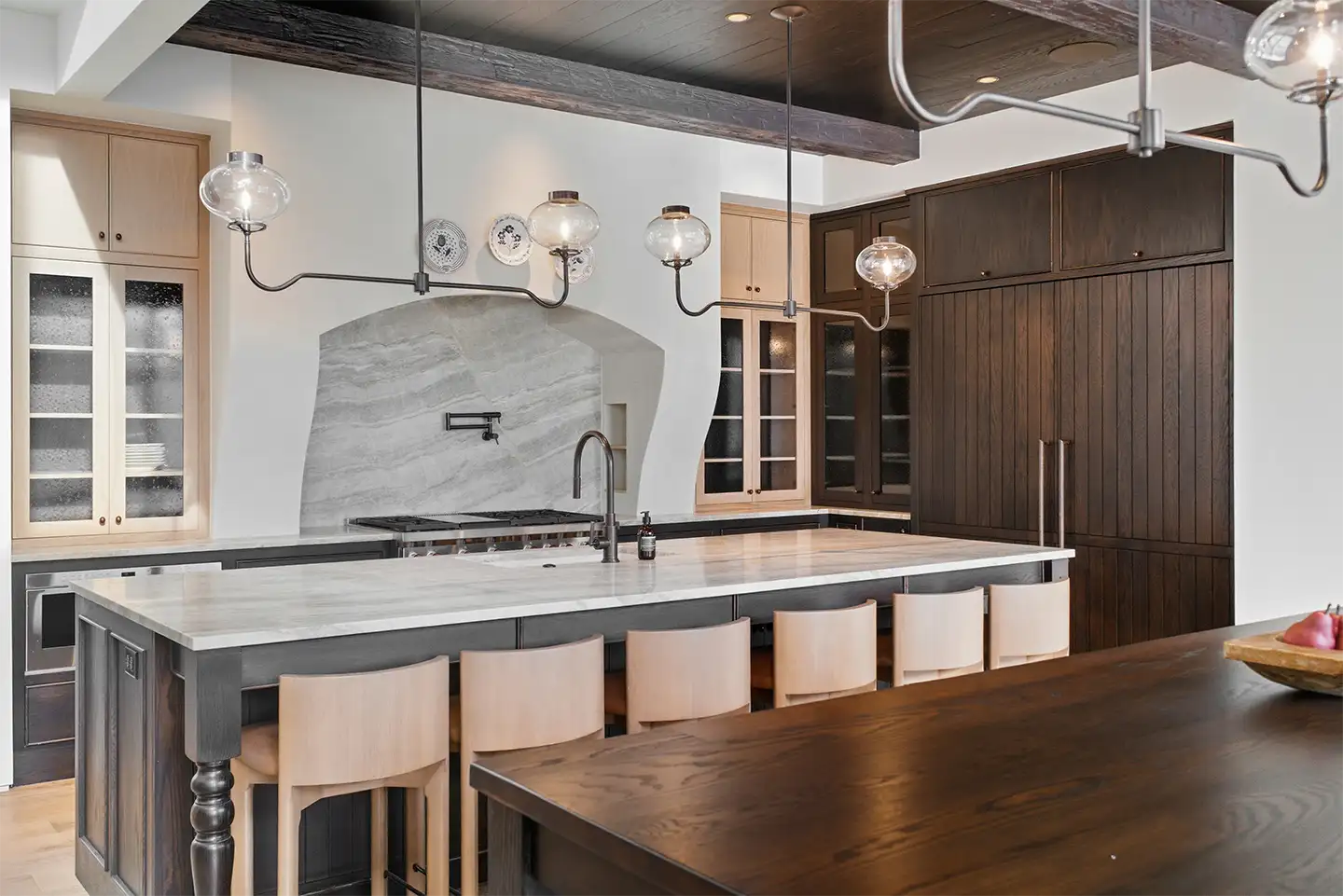Custom kitchen with mixed light and dark wood cabinetry, a marble island and backsplash, and glass globe pendant lighting.