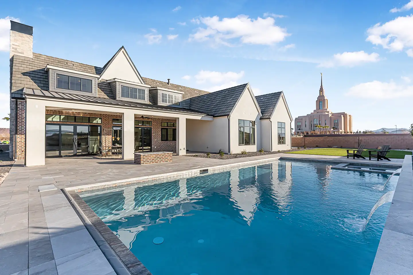 Rear exterior of a brick and stucco custom home with a pool and an LDS temple visible in the background under a blue sky.