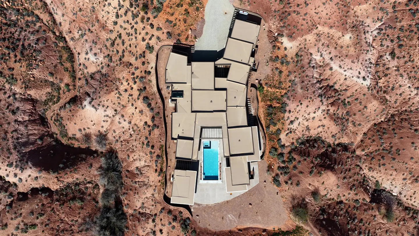 Aerial view of a sprawling modern desert home with a pool, built into rugged red rock terrain in Southern Utah.