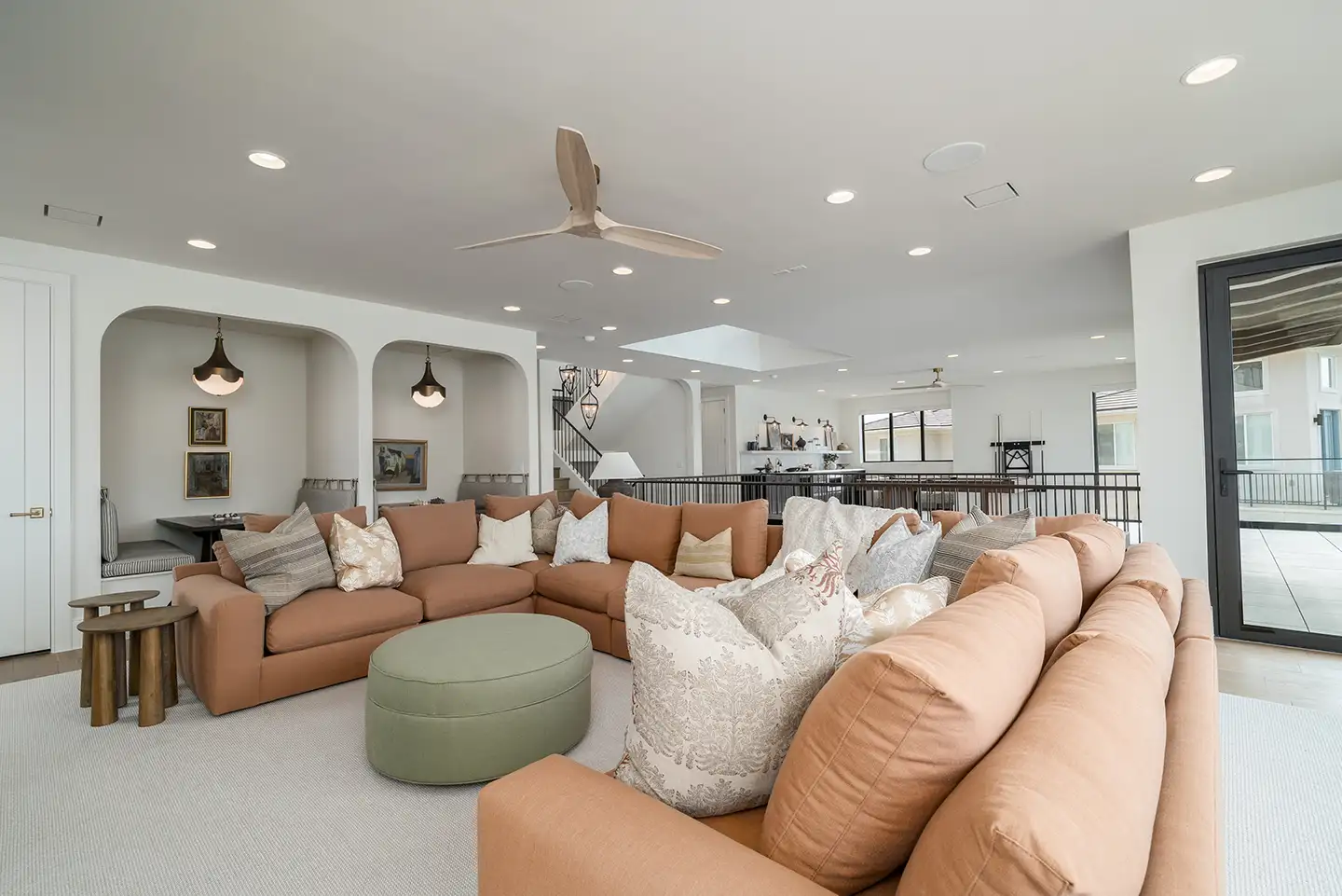 Upstairs great room with a terracotta sectional, green ottoman, arched art niches and a staircase, opening to a balcony.