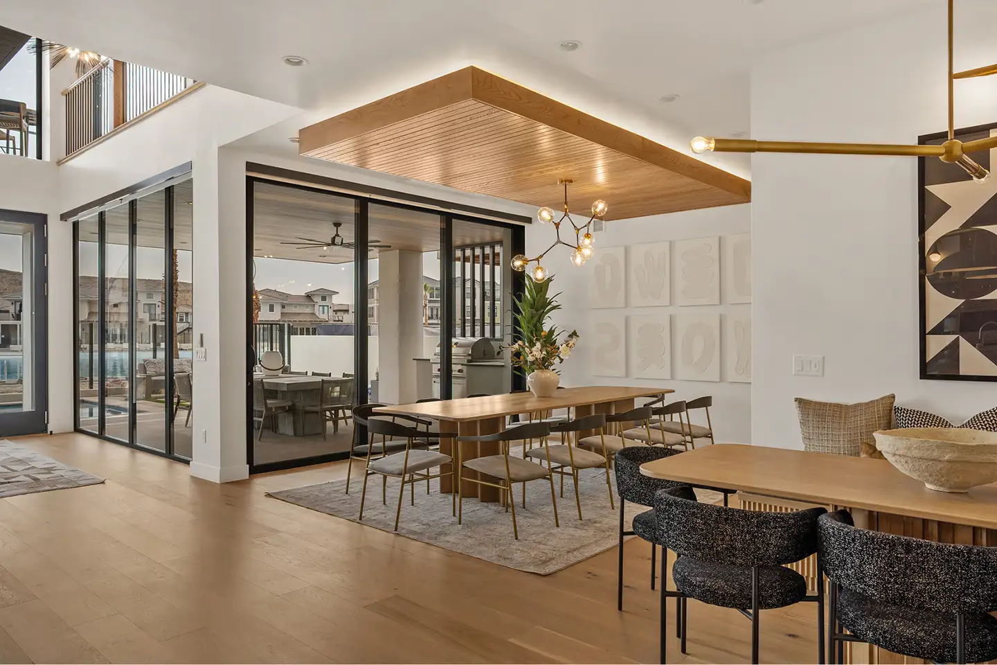 Open dining area with two tables, a sputnik chandelier and a wood-slat ceiling detail, with retractable glass doors to the patio and pool.