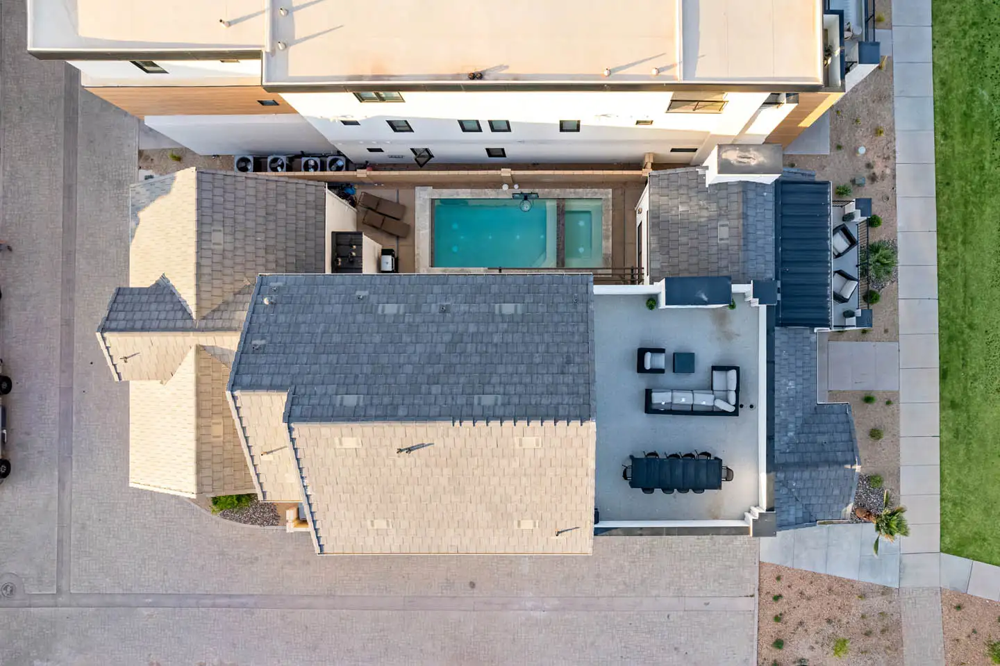 Aerial overhead view of a luxury home showing the rooftop, backyard pool and covered patio with outdoor dining and lounge areas.