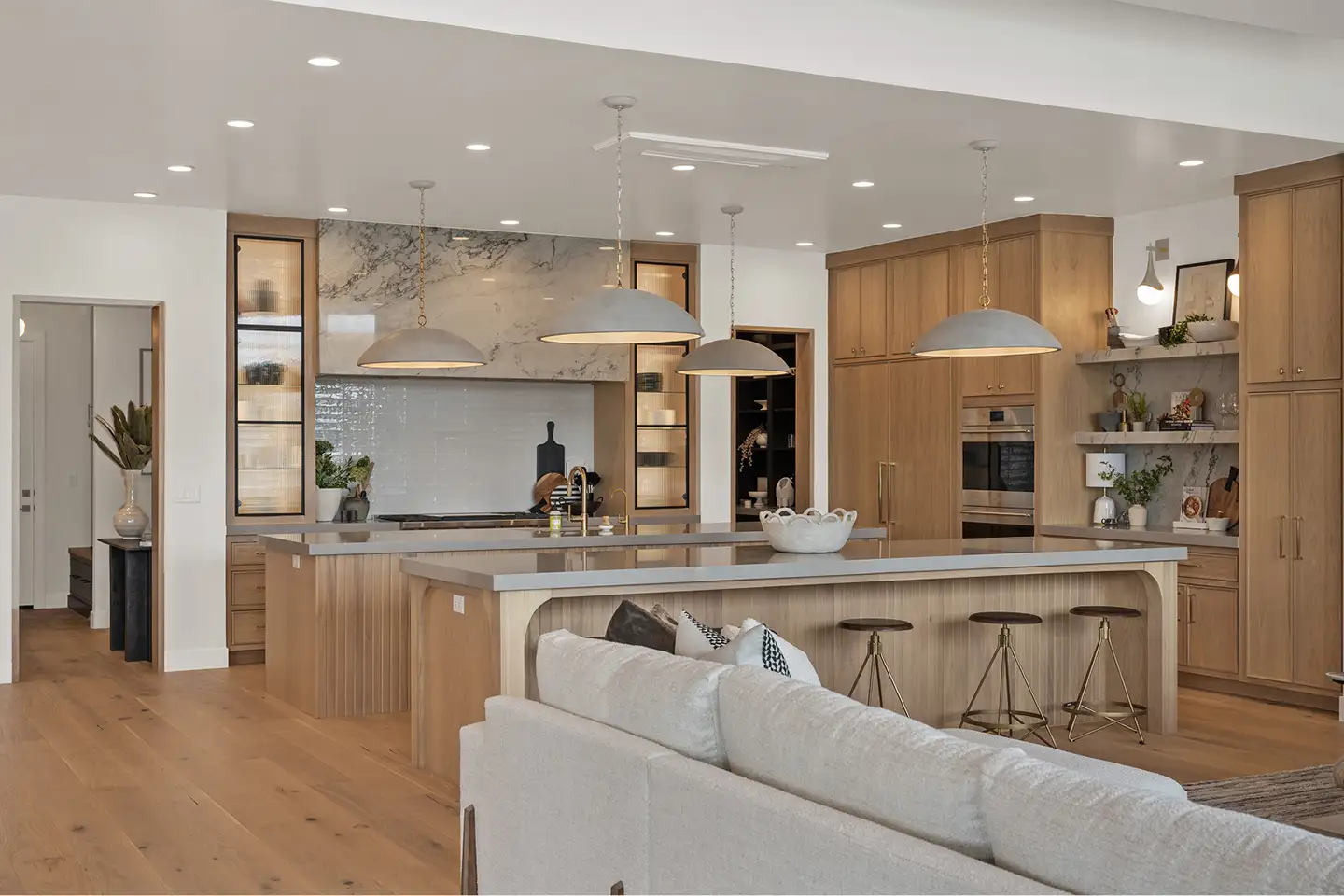 Open-concept kitchen with white-oak cabinetry, twin islands, a marble backsplash and dome pendant lights beside the living room.