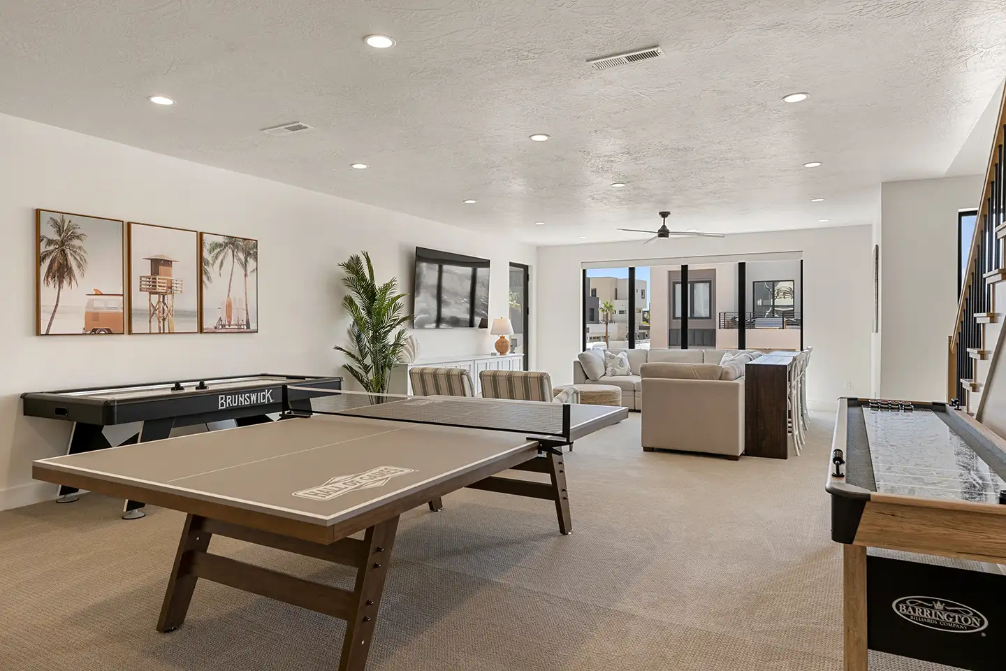 Multi-generational game room with a ping-pong table, air hockey and shuffleboard, plus lounge seating and coastal wall art.