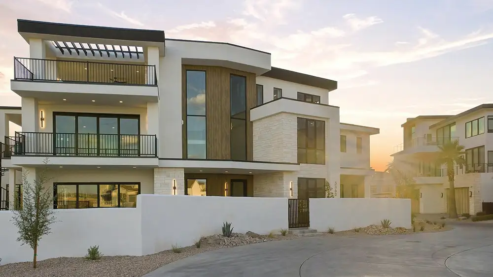 Three-story modern desert home at sunset with white stucco, wood accents, balconies, and a curved concrete driveway.