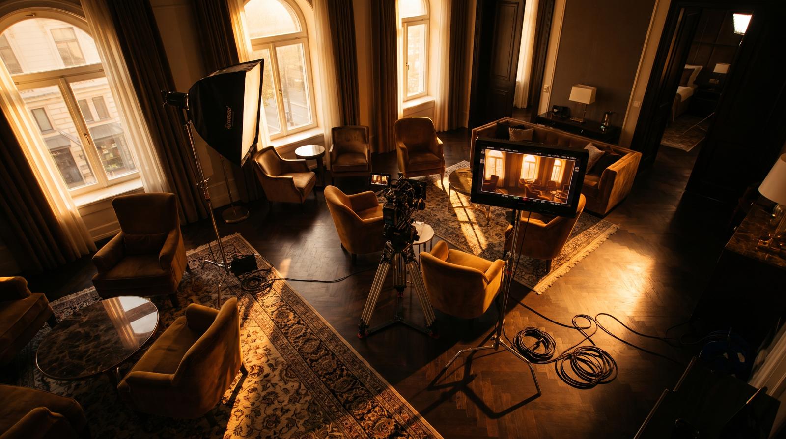 Film crew setting up a cinema camera and softbox in a luxury hotel suite for multi-purpose video production