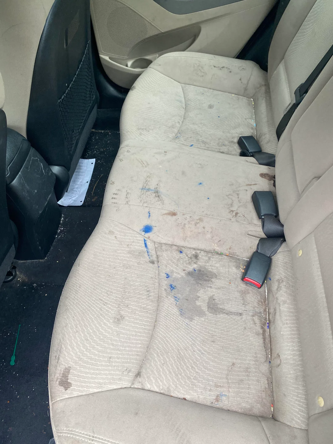 Beige car backseat with numerous stains and blue paint marks on the upholstery.