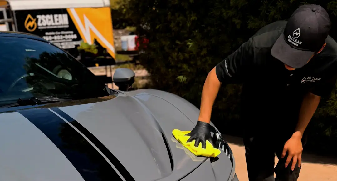 A ZS Clean detailer polishing a grey Ferrari, with the ZS Clean trailer behind