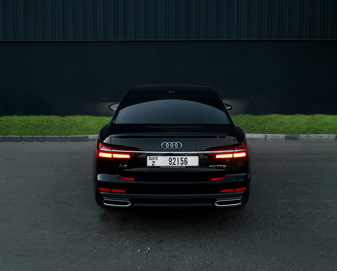 Black Audi A6 sedan with taillights on, parked against dark background