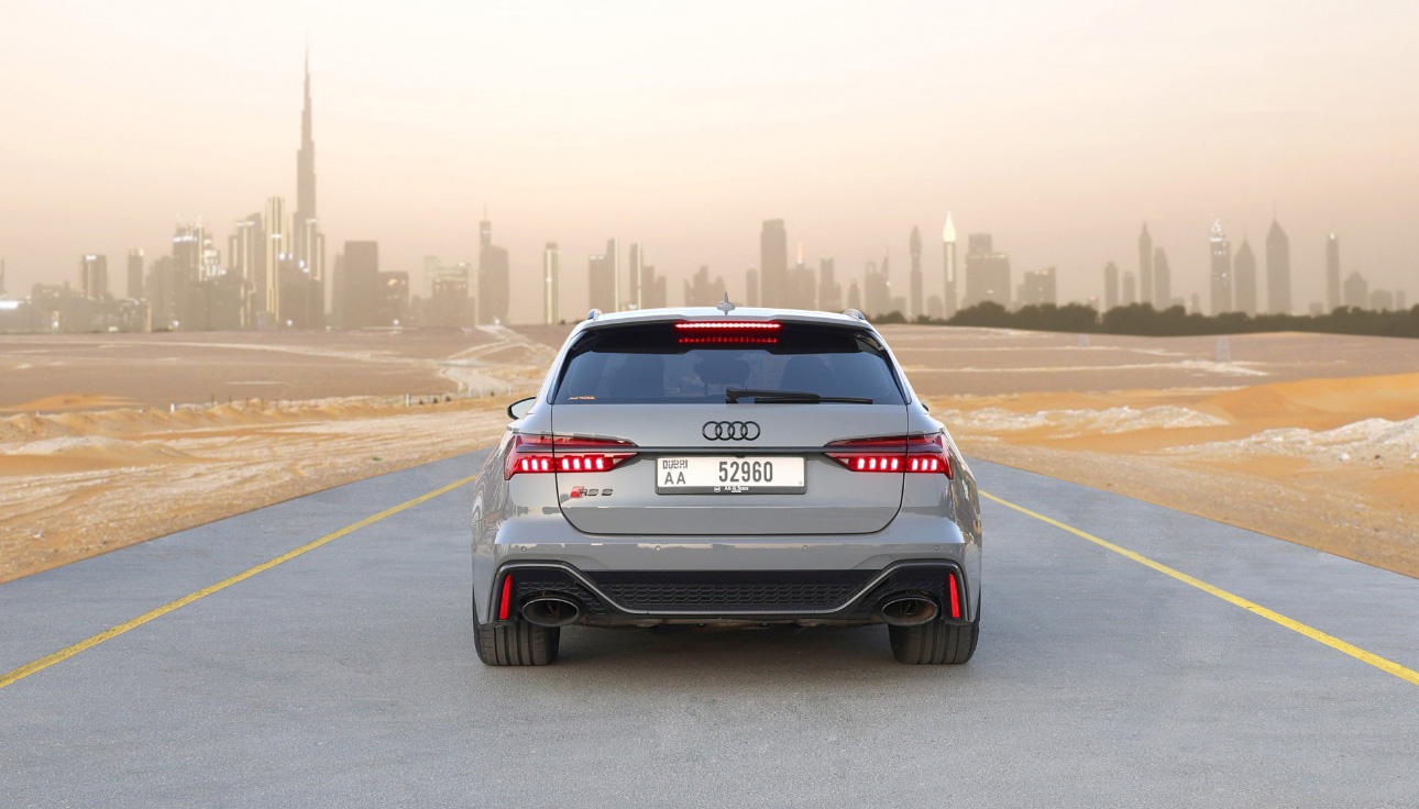 Silver Audi SUV on desert road with Dubai skyline in background