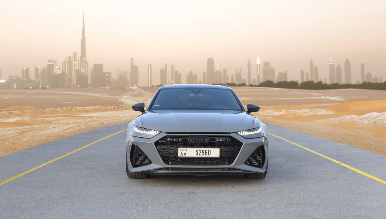 Gray Audi RS model on desert road with Dubai skyline at sunset