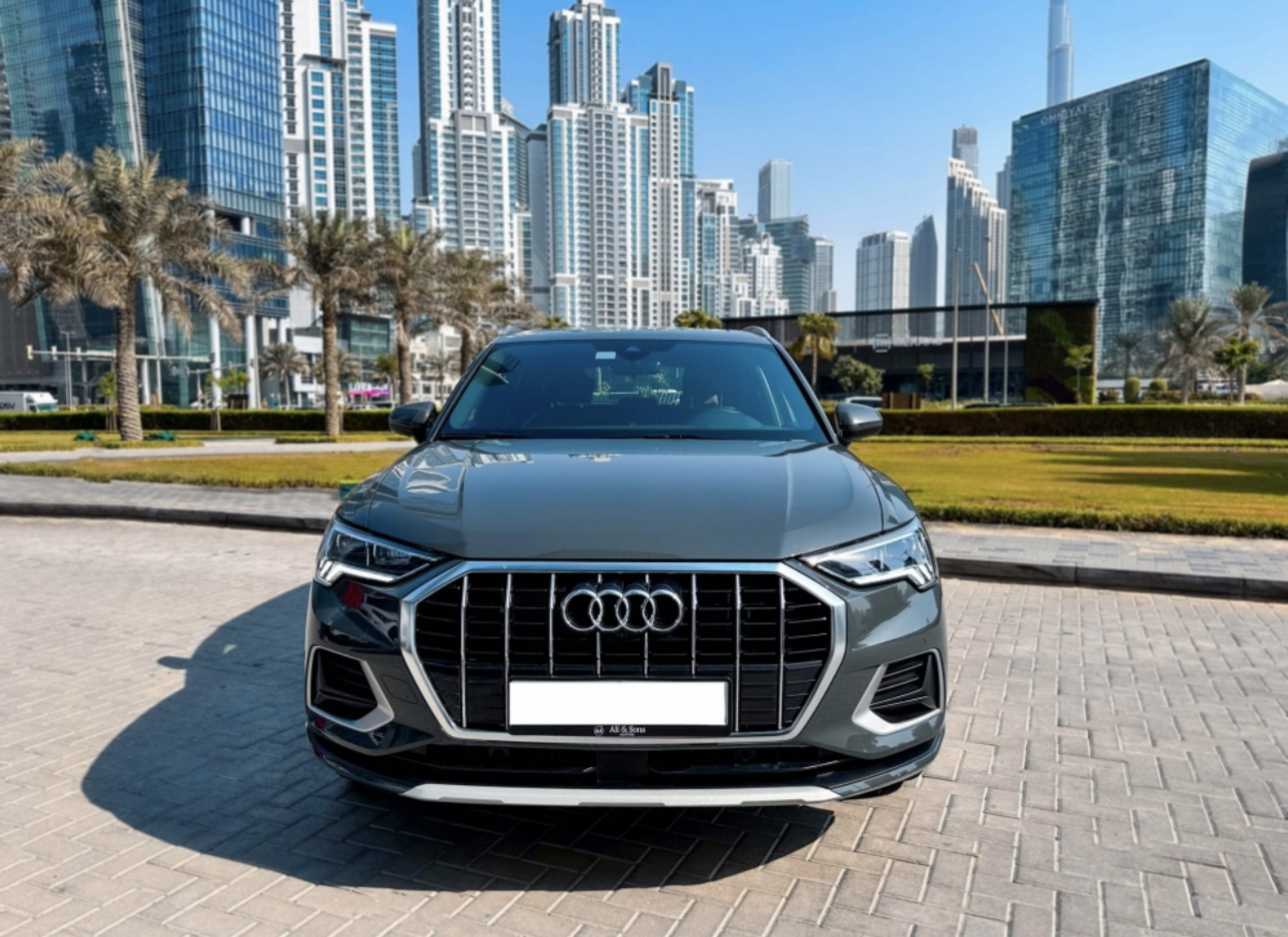 Gray Audi SUV parked in front of modern Dubai skyscrapers and palm trees