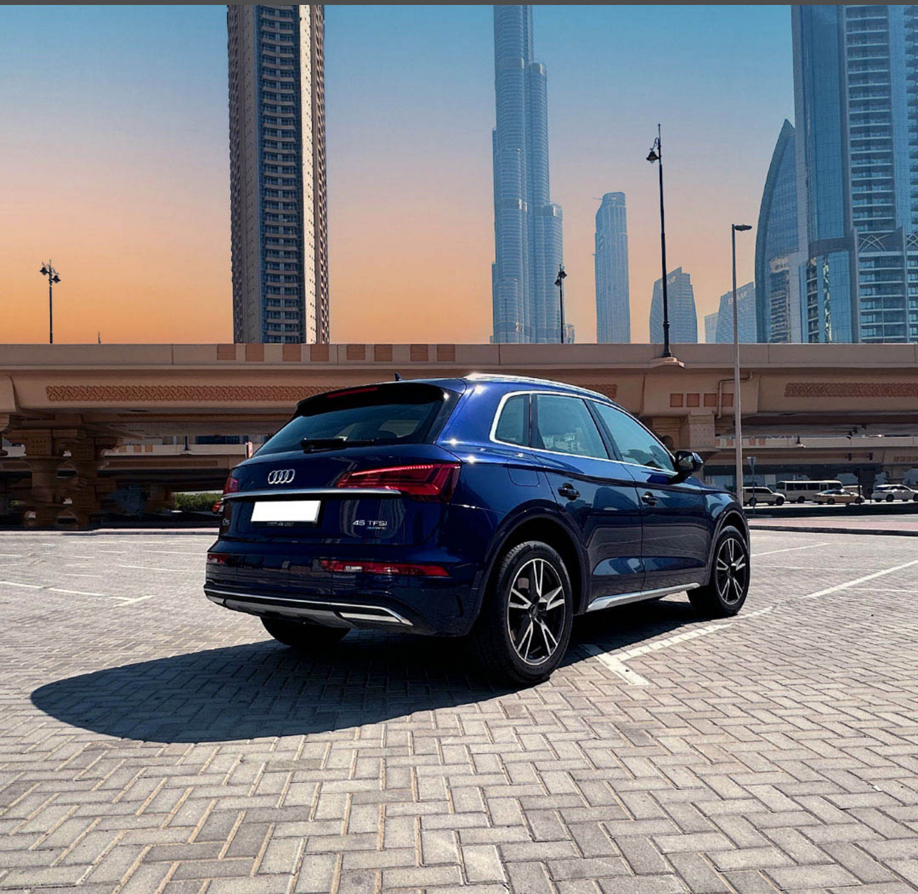 Blue Audi SUV parked in Dubai with skyscrapers and sunset backdrop