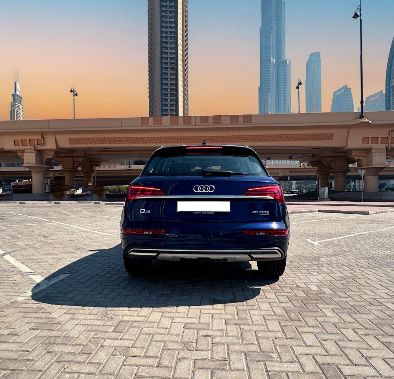 Blue Audi Q5 parked with Dubai skyscrapers in sunset background